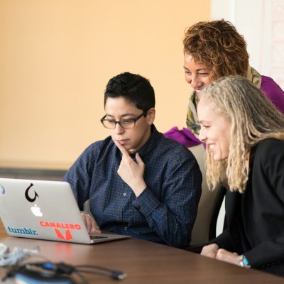 three women beside table looking at MacBook